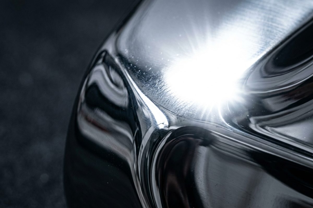 An extreme close-up of a curved, mirror-polished metal surface with a sharp, blown-out specular highlight in the center